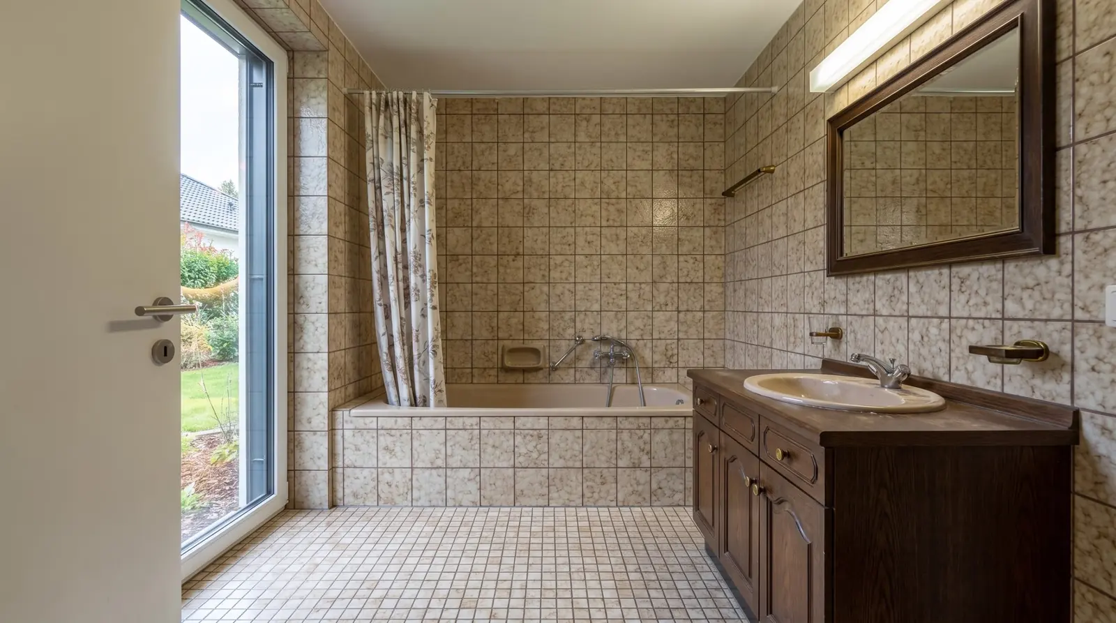 Dasselbe Bad vor der Sanierung mit braun gemusterten Plättli, Badewanne mit Vorhang und dunklem Holzmöbel